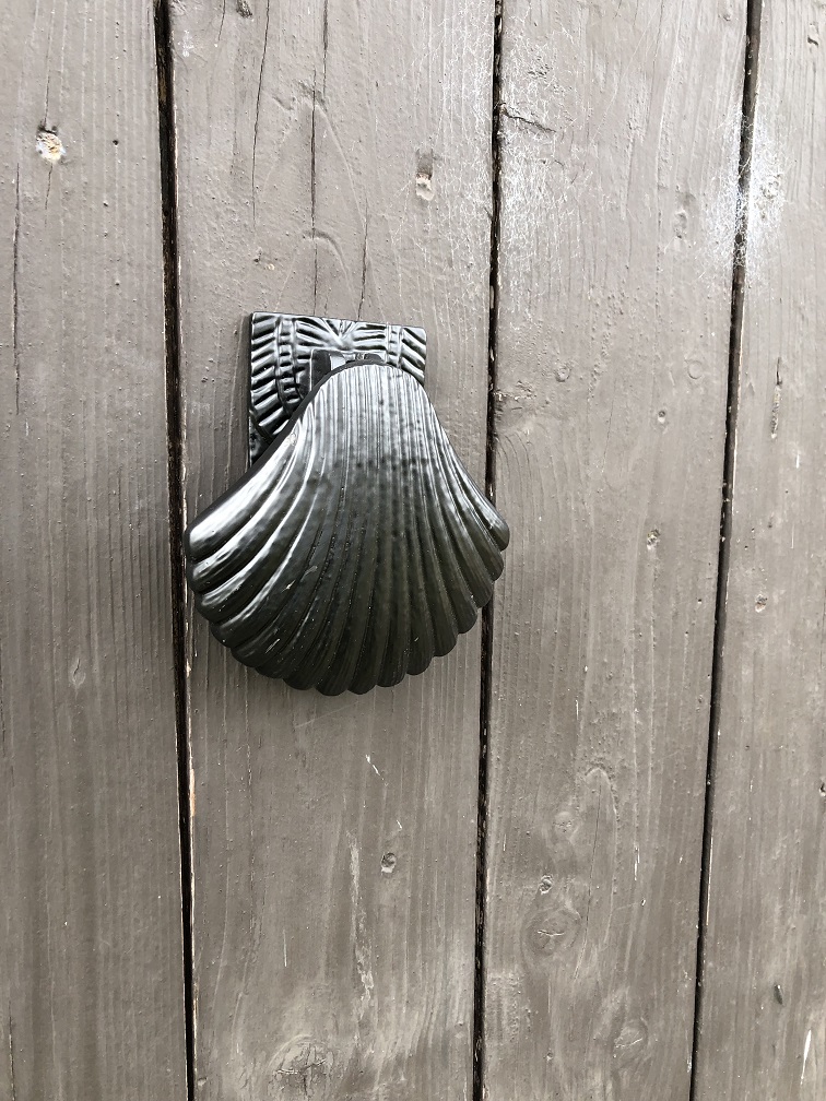 Dekorativer Türklopfer in Form einer Muschel, ganz aus schwarzem Metall.