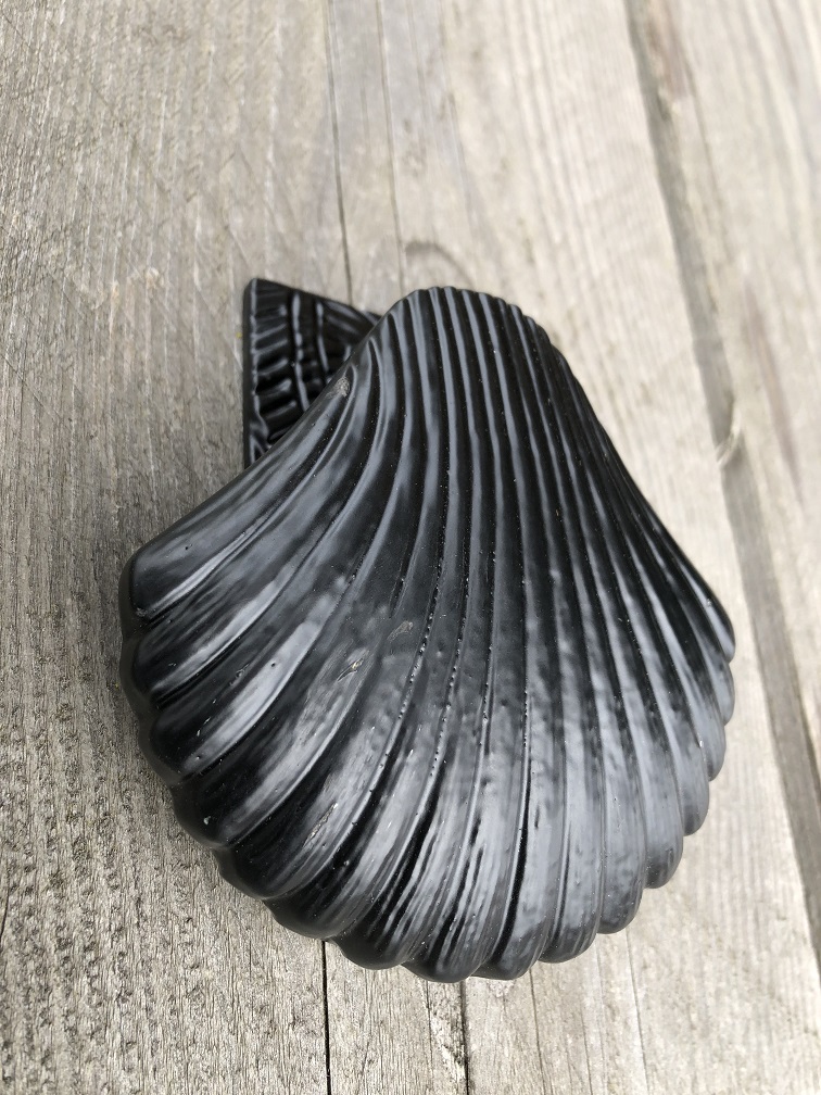 Decorative door knocker in the shape of a shell, all metal black.