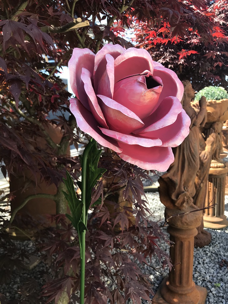 Een kunstwerkje, grote roze roos gemaakt van metaal, op steel