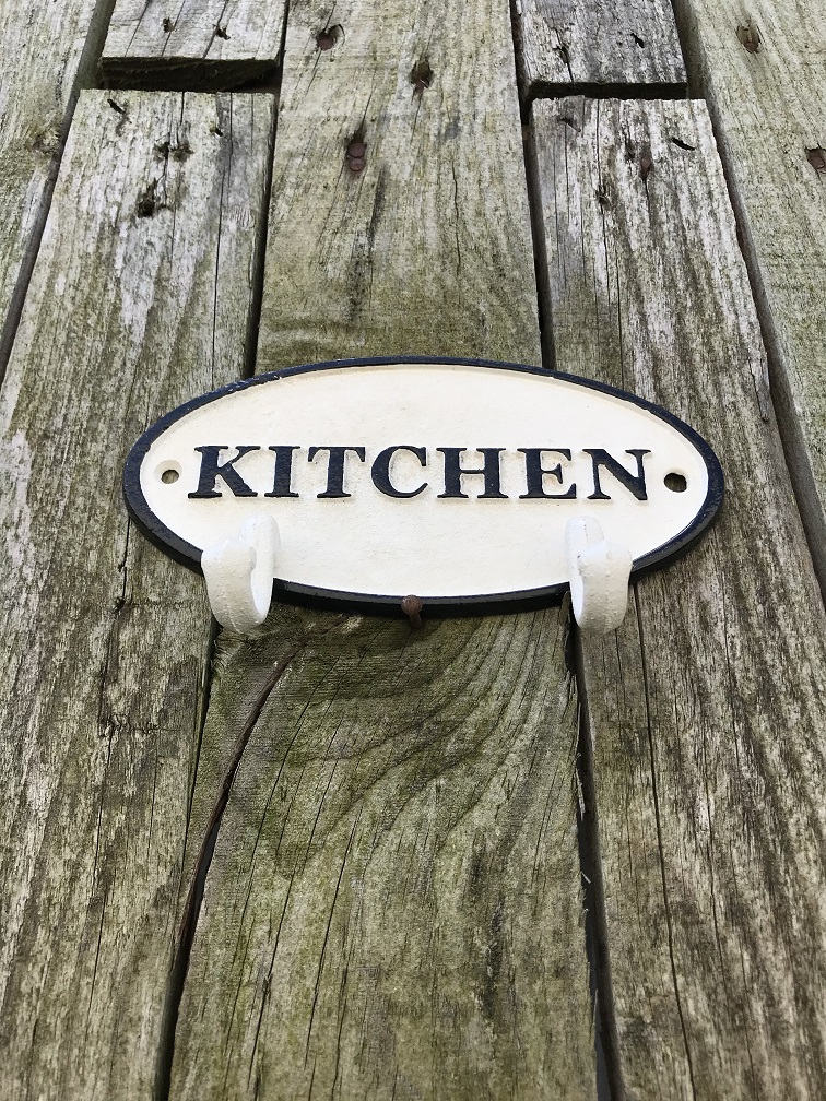 Een kapstok met 2 haken, bord met opschrift: ''KITCHEN'' als achtergrond, gietijzer