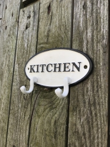 Een kapstok met 2 haken, bord met opschrift: ''KITCHEN'' als achtergrond, gietijzer