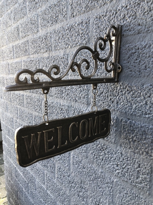 Uithangbord-wandbord aan mooie handbeugel, metaal, bronskleur, met de tekst: WELCOME.