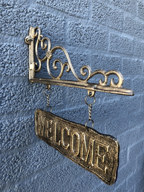 Uithangbord-wandbord aan mooie handbeugel, metaal, bronskleur, met de tekst: WELCOME.