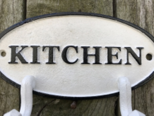 Een kapstok met 2 haken, bord met opschrift: ''KITCHEN'' als achtergrond, gietijzer