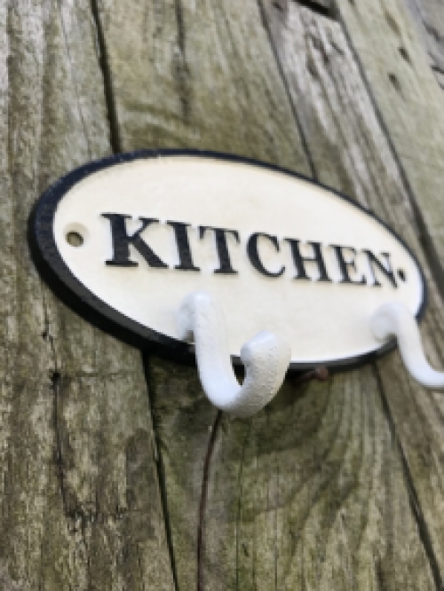 Een kapstok met 2 haken, bord met opschrift: ''KITCHEN'' als achtergrond, gietijzer