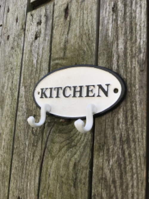 Een kapstok met 2 haken, bord met opschrift: ''KITCHEN'' als achtergrond, gietijzer