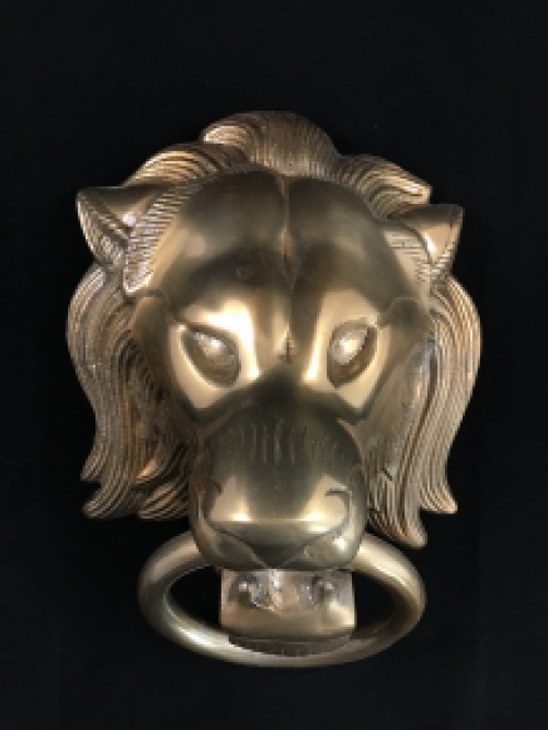 A lion's head, made of aluminum in a brass color, as a door knocker