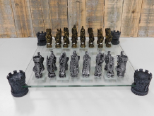 Een schaakspel met als thema: '' ridder-draken'', fraaie schaakstukken als middeleeuws e ridders op glazen schaakbord met torens.