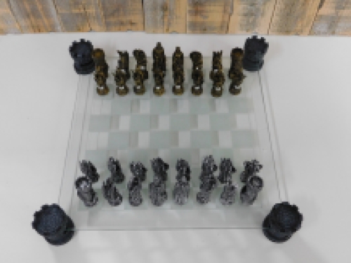 Een schaakspel met als thema: '' ridder-draken'', fraaie schaakstukken als middeleeuws e ridders op glazen schaakbord met torens.