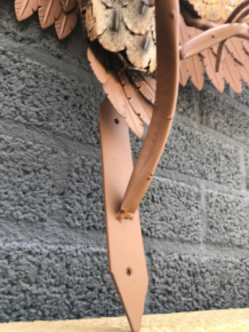 Een metalen sculptuur van een uil op een tak, voor aan de muur