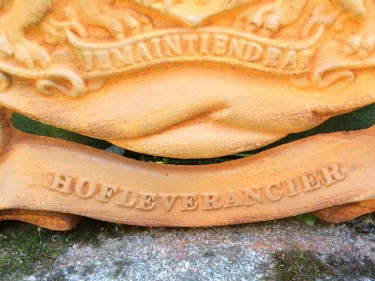 Gietijzeren wandornament, zwaar uitgevoerd met de spreuk: Je maintiendrai (ik zal handhaven), hofleverancier