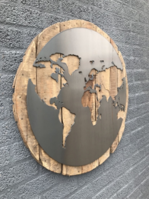 Een groot wandornament, gemaakt van hout met hierop een wereld, zee van metaal
