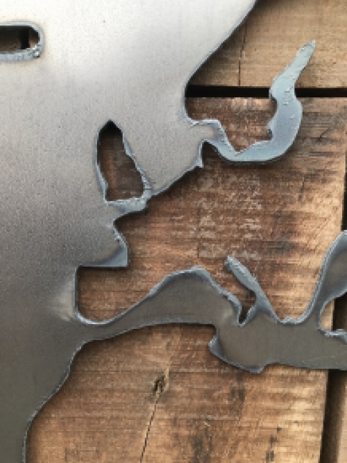 Een groot wandornament, gemaakt van hout met hierop een wereld, zee van metaal